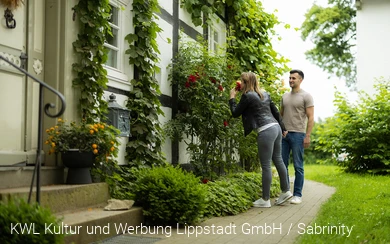 Eine Frau atmet den Duft einer Rose vor einem alten Fachwerkhaus am Stift Cappel im Lippstädter Ortsteil Cappel ein. Copyright: KWL Kultur und Werbung Lippstadt GmbH / Sabrinity