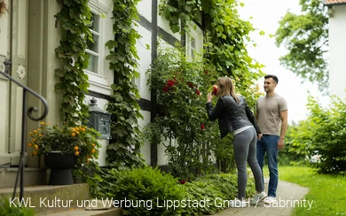 Eine Frau atmet den Duft einer Rose vor einem alten Fachwerkhaus am Stift Cappel im Lippstädter Ortsteil Cappel ein. Copyright: KWL Kultur und Werbung Lippstadt GmbH / Sabrinity