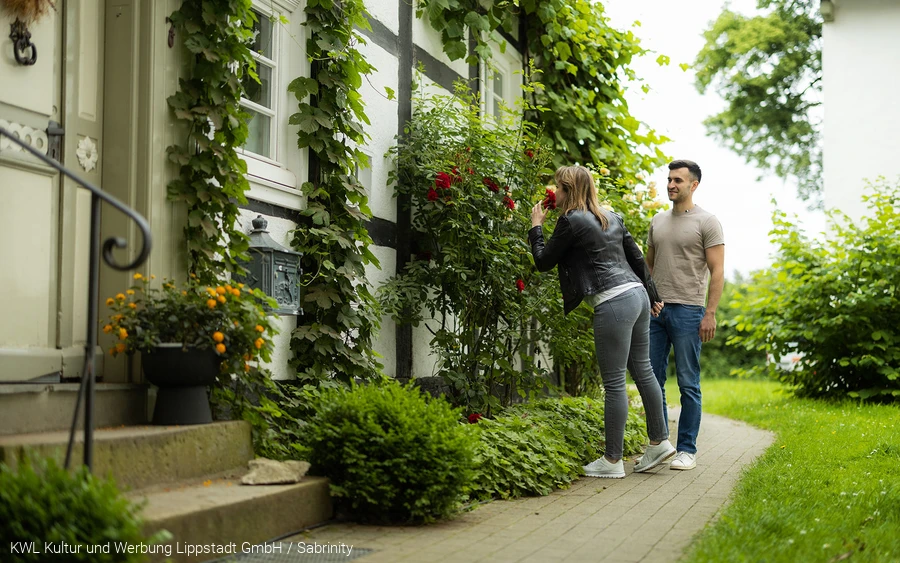 Eine Frau atmet den Duft einer Rose vor einem alten Fachwerkhaus am Stift Cappel im Lippstädter Ortsteil Cappel ein. Copyright: KWL Kultur und Werbung Lippstadt GmbH / Sabrinity
