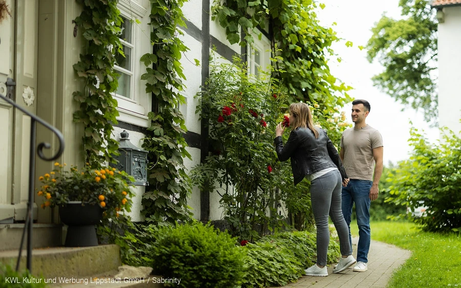 Eine Frau atmet den Duft einer Rose vor einem alten Fachwerkhaus am Stift Cappel im Lippstädter Ortsteil Cappel ein. Copyright: KWL Kultur und Werbung Lippstadt GmbH / Sabrinity