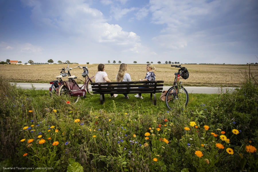Drei Frauen sitzen auf einer Bank umgeben von Feldern. Sie unterhalten sich. Neben der Bank stehen Fahrr&auml;der. Foto: Sauerland Tourismus e.V./ Foto: Sabrina Voss (sabrinity)
