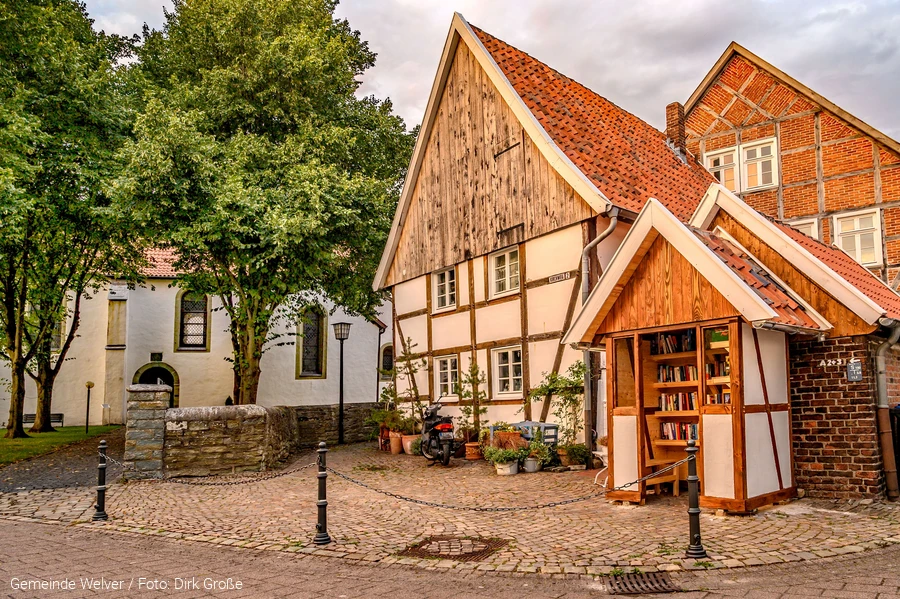 Alte, kleine Fachwerkh&auml;user in Kirchwelver. Im Hintergrund ist die Klosteranlage zu sehen. Im Vordergrund ist ein B&uuml;cher-Tausch-Schrank in Fachwerk-Optik. Copyright: Gemeinde Welver Foto: Dirk Gro&szlig;e